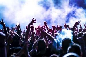 siluetas de una multitud durante un concierto frente a las luces brillantes del escenario, cada uno tiene las manos levantadas en el aire bailando