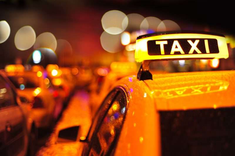 Taxi manejando durante la noche con un enfoque en la señal de luz amarilla y negra de los taxis