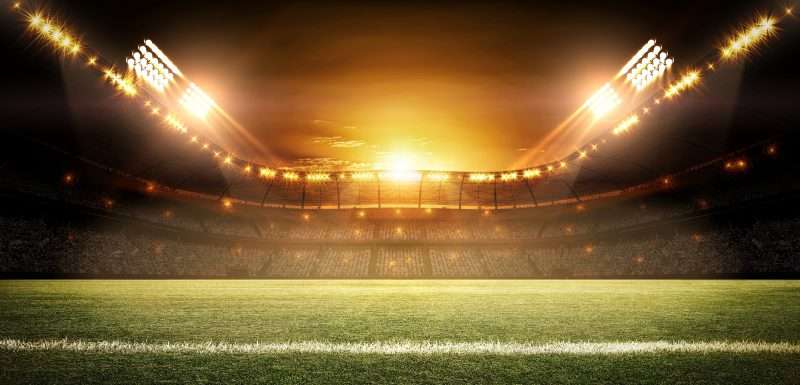 Estadio de fútbol con el césped verde, las gradas y las luces de los campos con un filtro naranja.