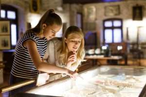 Una niña y una mujer observando con interés objetos de arte bajo vidrio en un museo de Medellín utilizando guías de visita