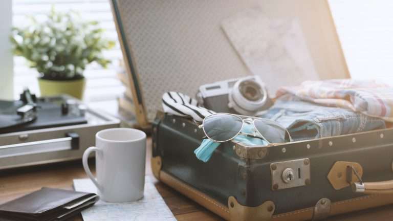 Viajera empacando su maleta antes de salir de viaje: maleta vintage abierta con ropa, gafas de sol, cámara y tocadiscos vintage
