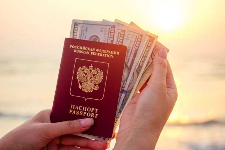 Mano sosteniendo un pasaporte y billetes en la playa frente al mar durante la puesta de sol.
