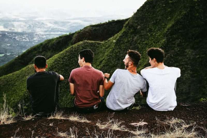 Group of 4 young caucasian men sitting at a top of a mountain near Medellin admiring the landscape and laughing together