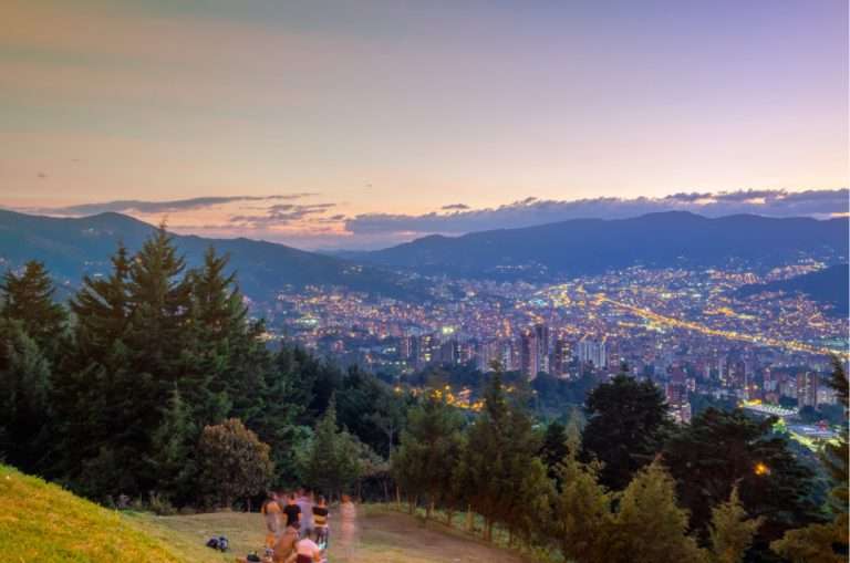 A couple is looking at the mountains of Medellin and the lights of the city during sunset at Las Palmas, one of the best viewpoints of Medellin