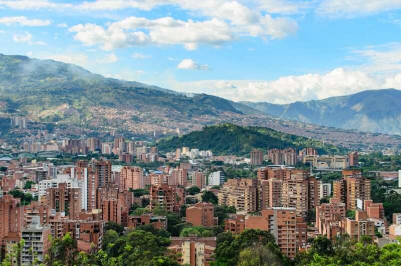 Red brick buildings on lush green mountains under pale blue skies - Medellin, Colombia